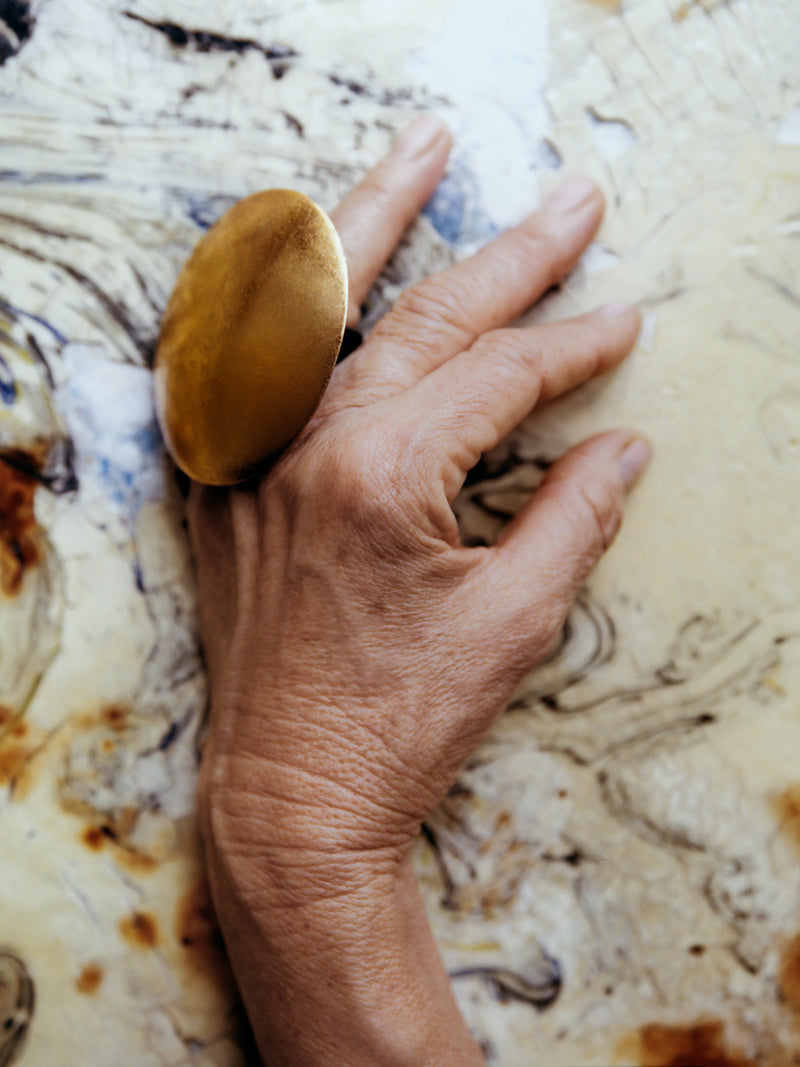 hand wearing a large goldfoil ring on a marble background