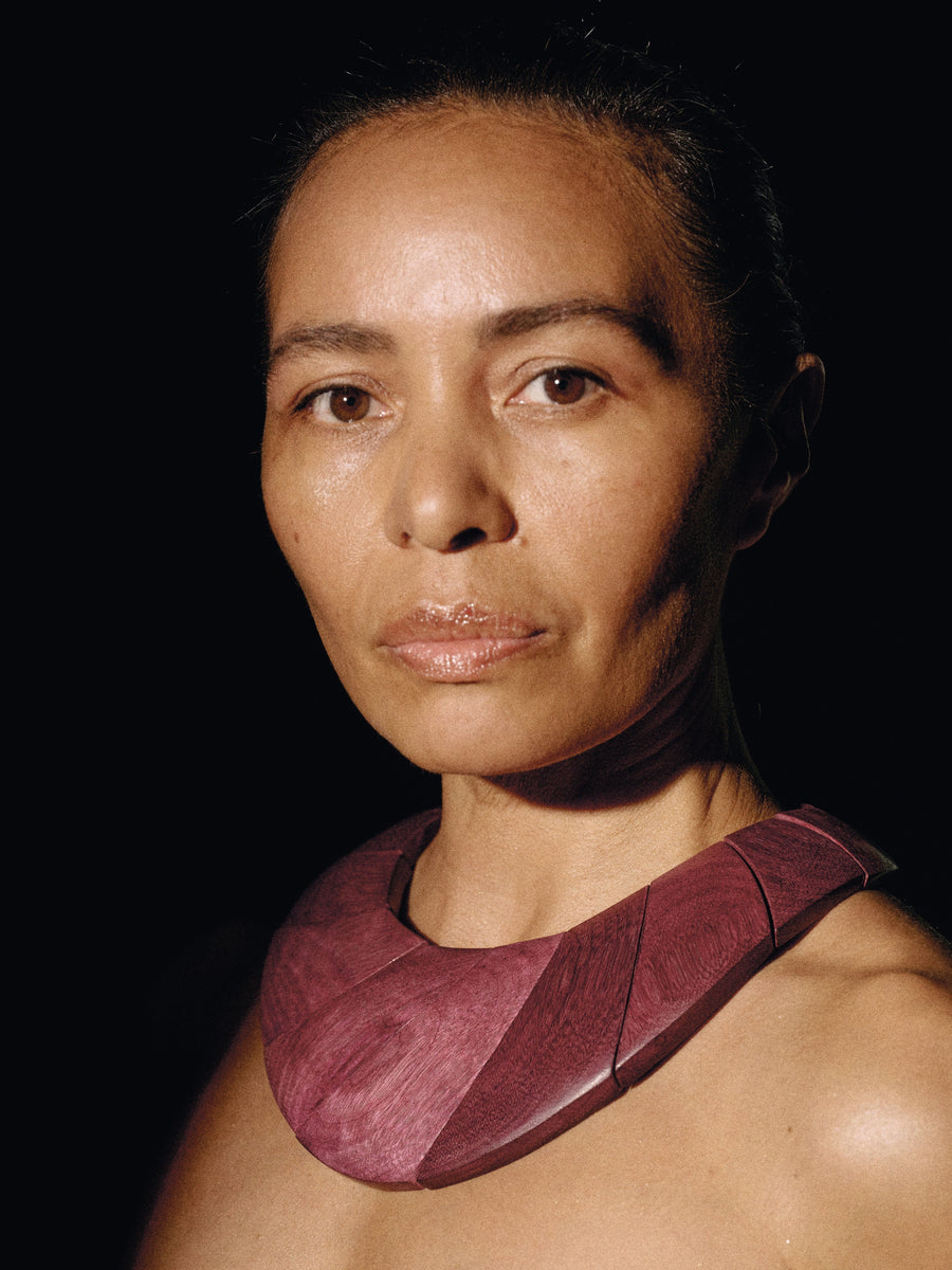 Woman wearing a dark red necklace against a black background