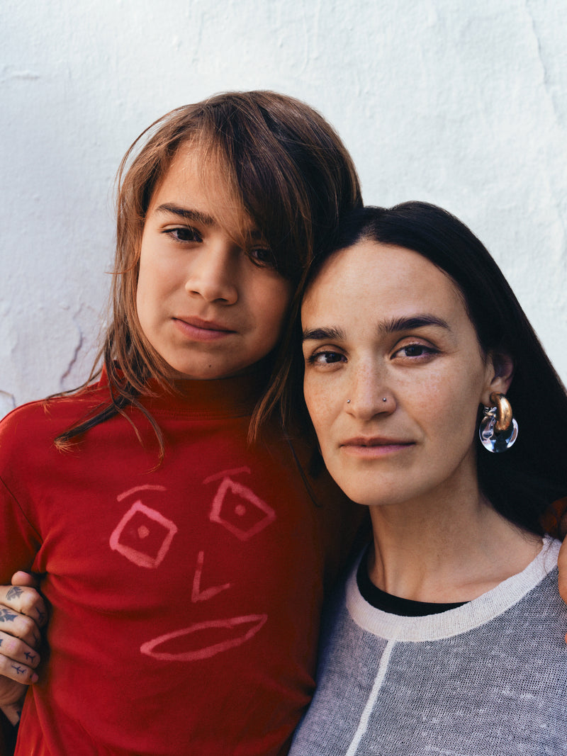 Two people standing close together against a light-colored wall.