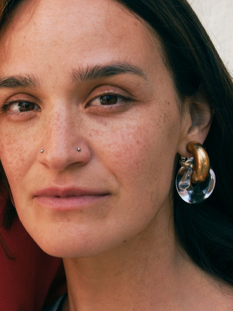 Close-up of a person wearing large hoop earrings with gold and clear stones.