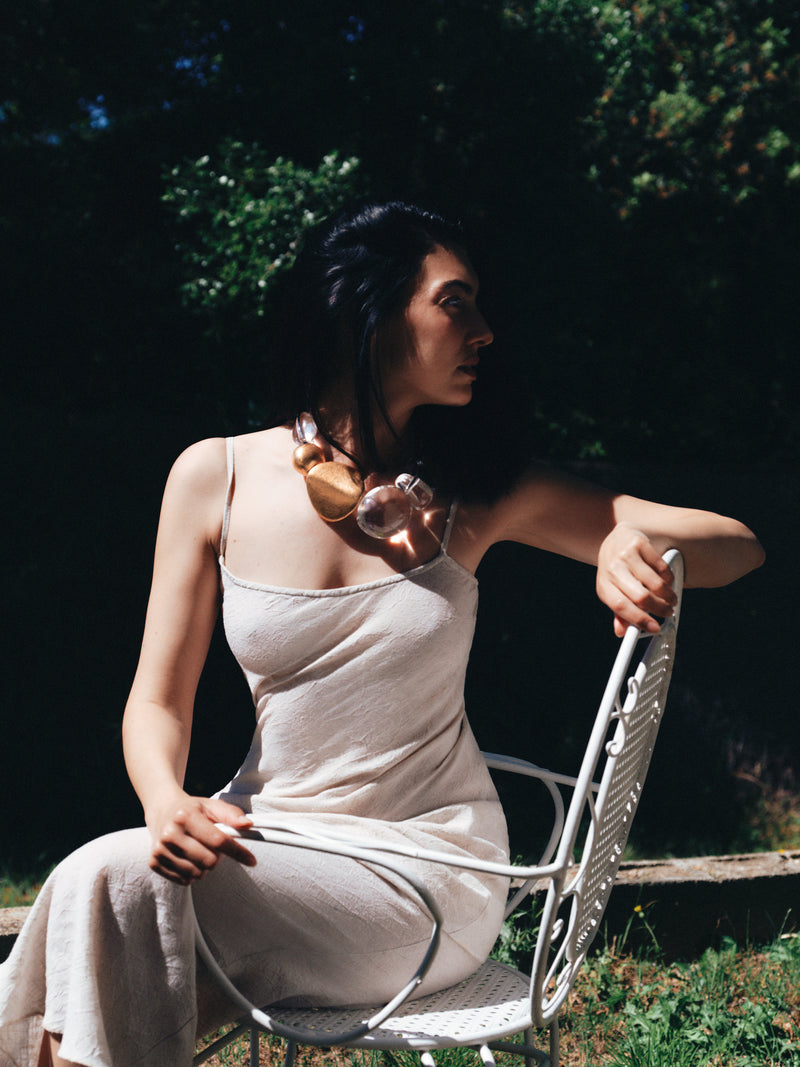 Woman in a light dress sitting on a chair outdoors with a dark background