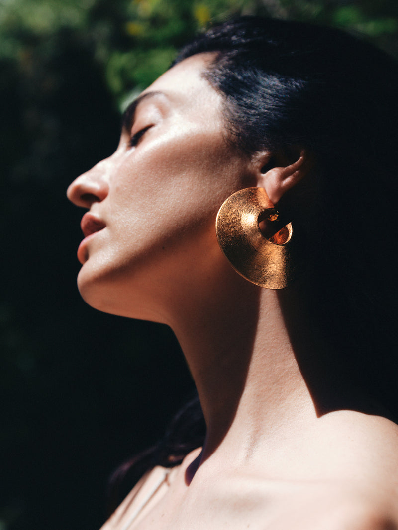 Woman wearing gold earrings with a blurred natural background