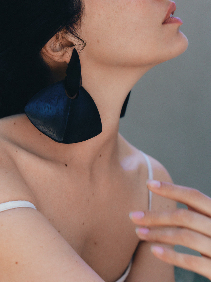Close-up of a person wearing large black earrings with a neutral background