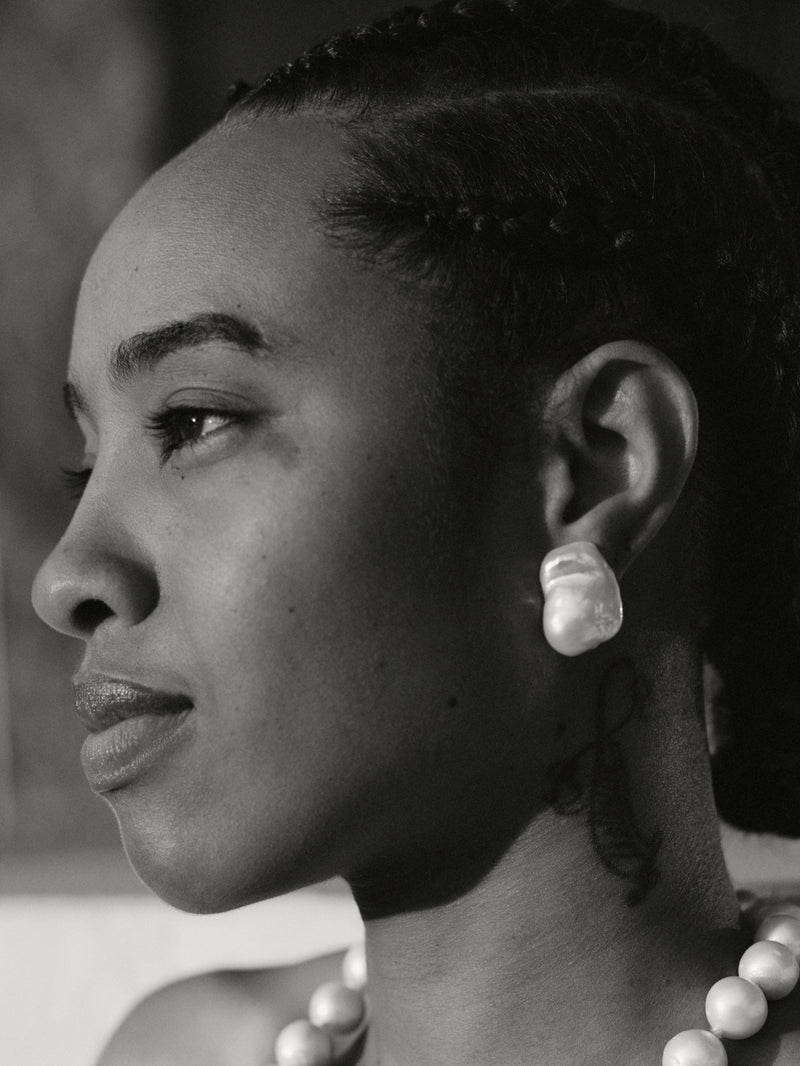 Black and white portrait of a woman wearing a pearl necklace and earrings.