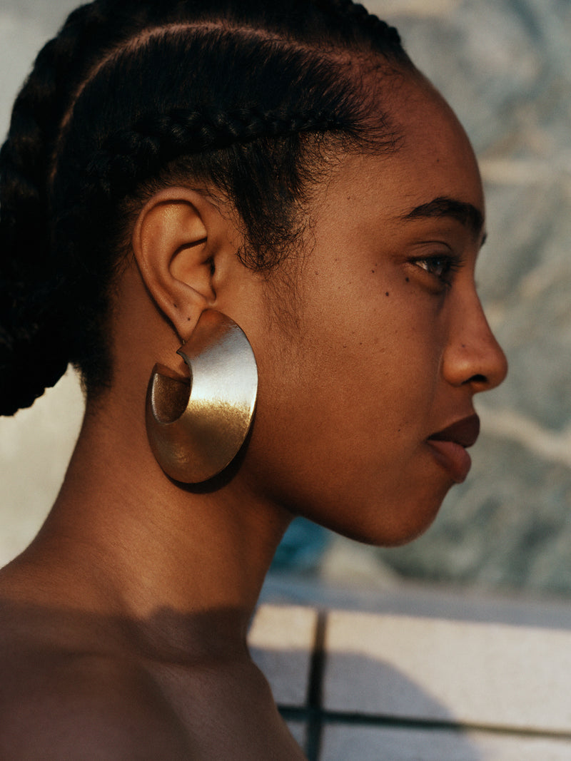 Woman wearing large gold hoop earrings with a blurred background