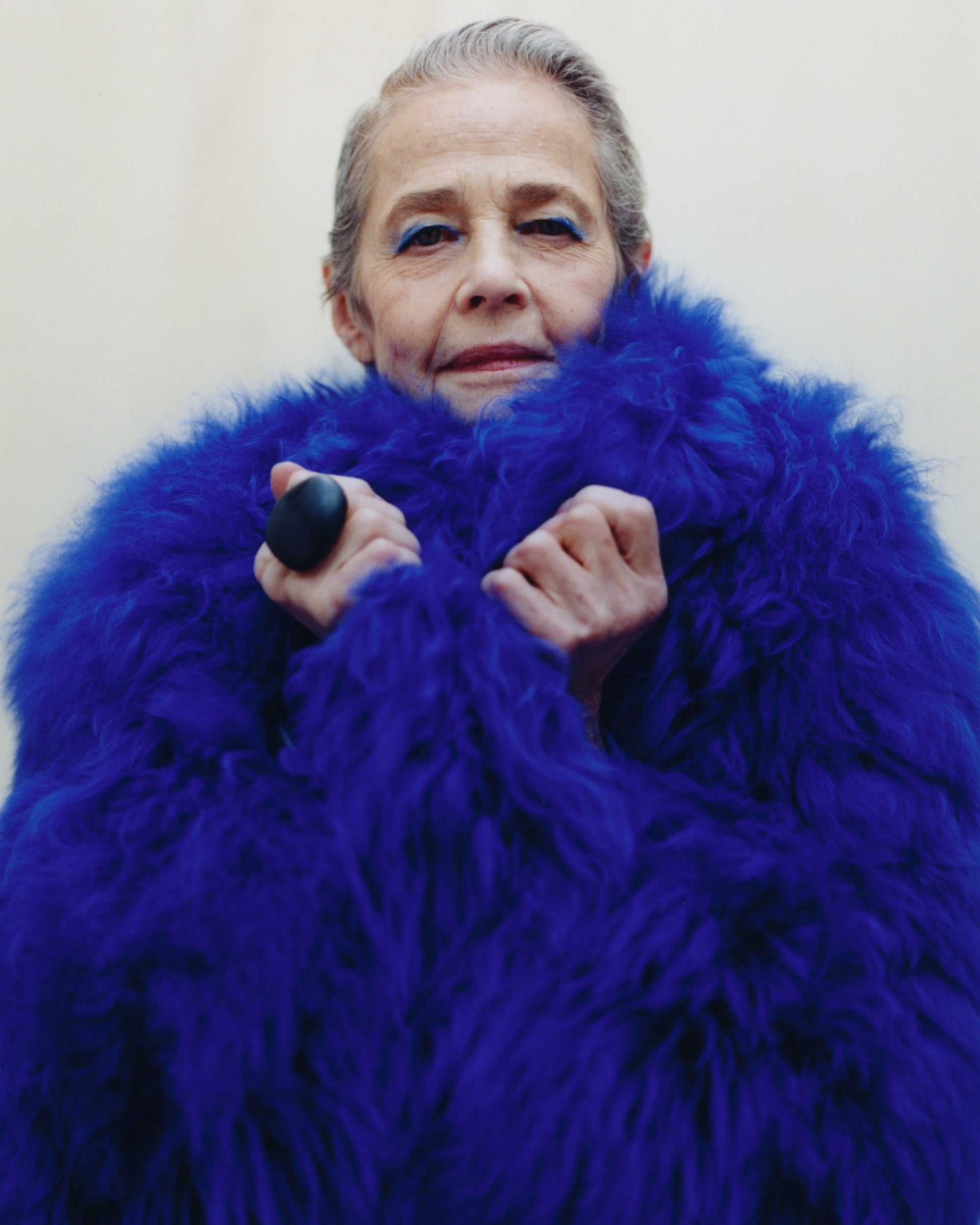Person wearing a bright blue fur coat against a plain background