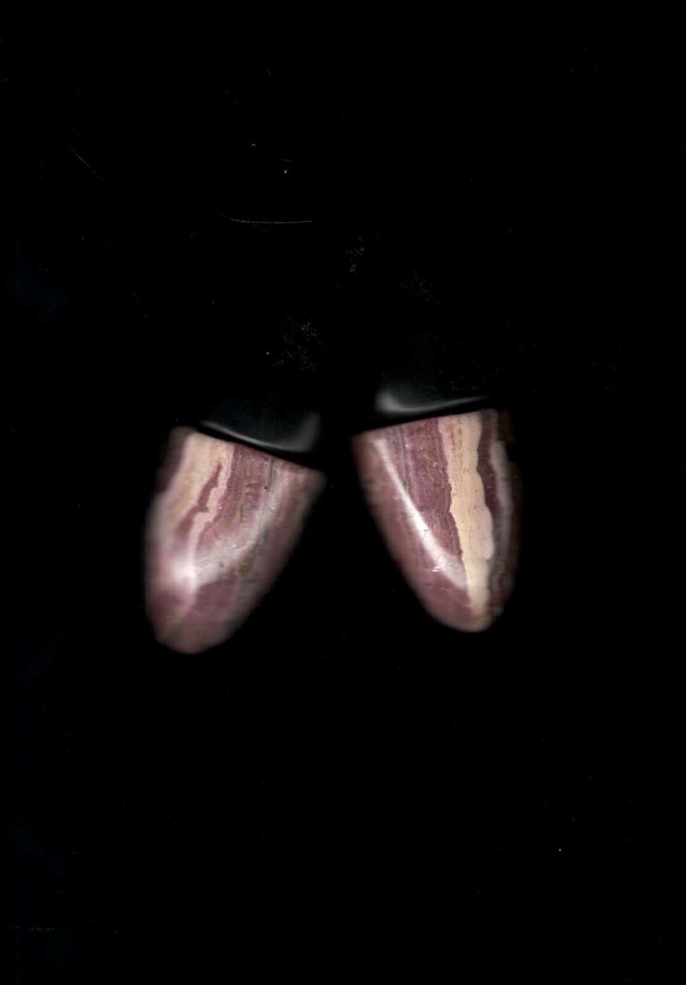 A blurry image of pair of earrings with black oval tops and marbled pink and white stone lower halves, shown on a black background