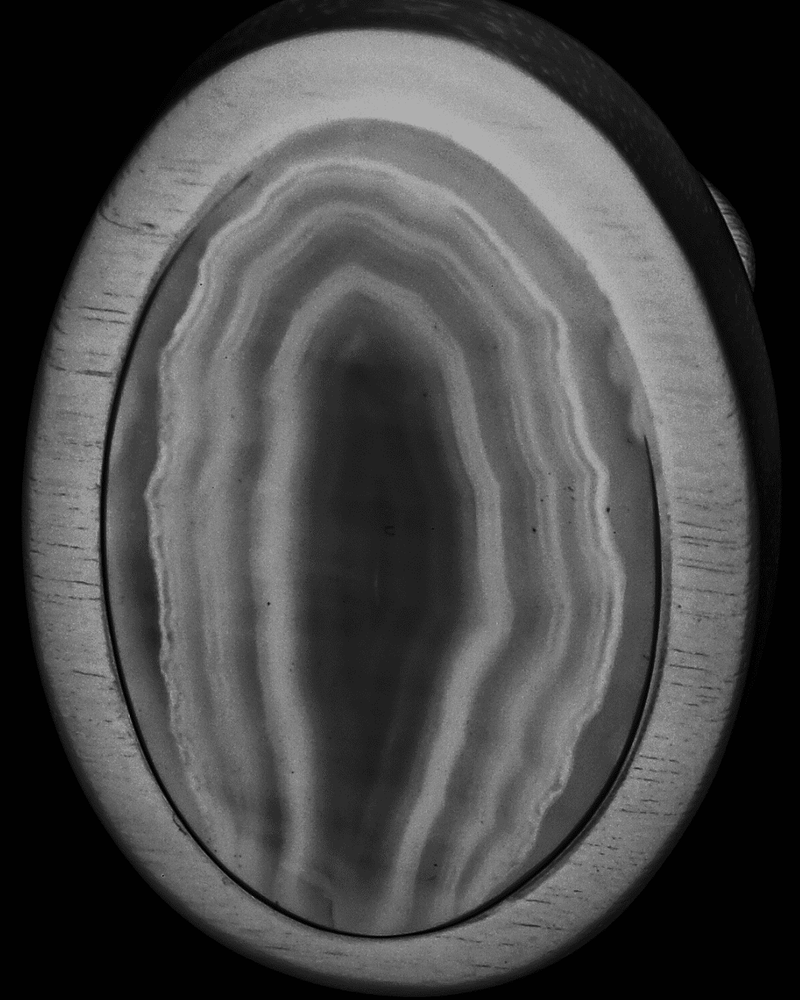 An oval-shaped cabochon gemstone featuring concentric bands of agate or obsidian, shown against a solid black background.