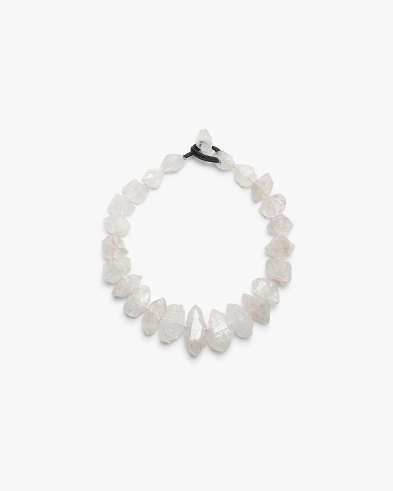 A beaded stretch necklace made of  white raw crystal chips, tied with a black elastic band, shown on a plain light gray background.