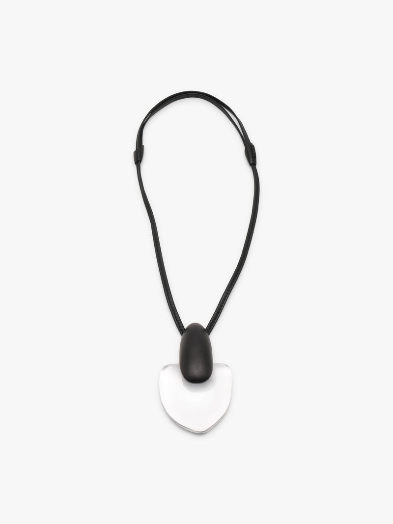 A pendant featuring a smooth, teardrop-shaped black pendant resting on a larger, polished transparent heart-shaped stone, suspended from a black leather cord, shown against a plain light gray background.