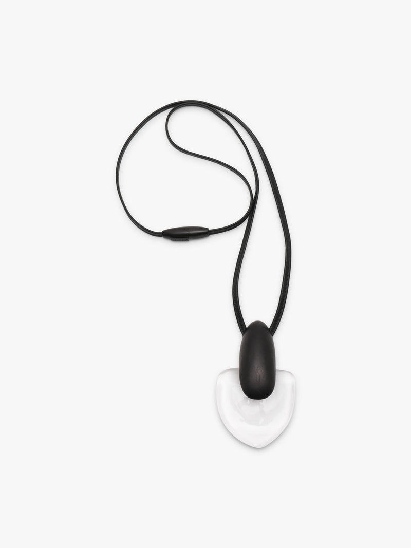 A pendant featuring a smooth, teardrop-shaped black pendant resting on a larger, polished transparent heart-shaped stone, suspended from a black leather cord, shown against a plain light gray background.