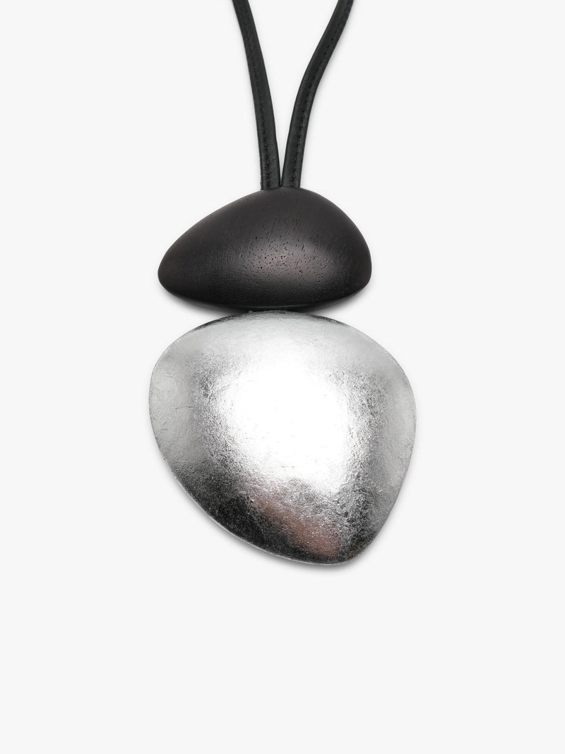 A black and silver dual-tone pendant with a black leather strap, displayed against a clean, light gray background.