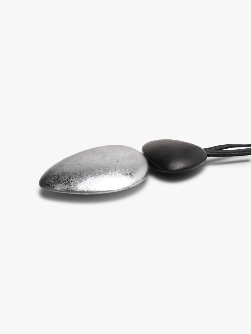 A black and silver dual-tone pendant with a black leather strap, displayed against a clean, light gray background.
