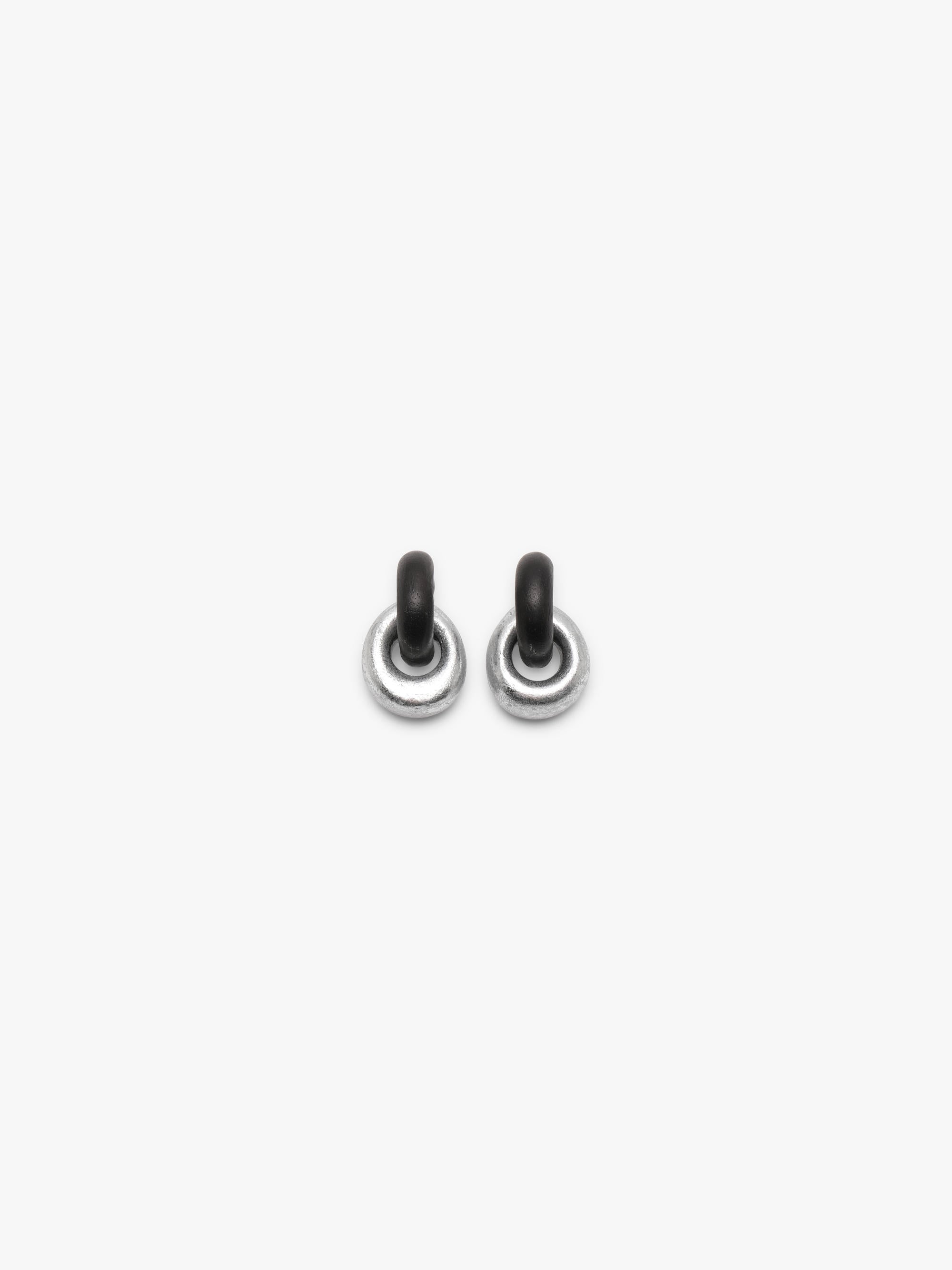 A pair of small silver-toned stud earrings with dark, possibly black, curved tops, shown against a plain light gray background.