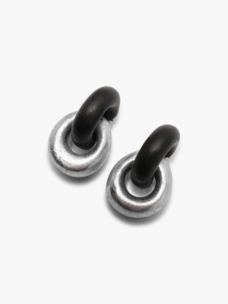 A pair of small silver-toned stud earrings with dark, possibly black, curved tops, shown against a plain light gray background.