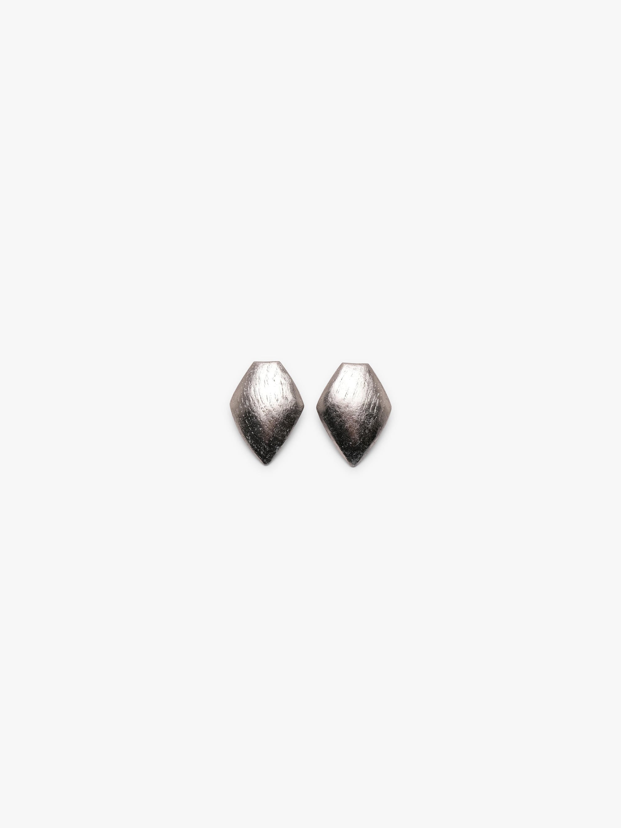 A pair of textured, metallic silver geometric stud earrings with a faceted, diamond-like shape, shown against a plain light gray background.