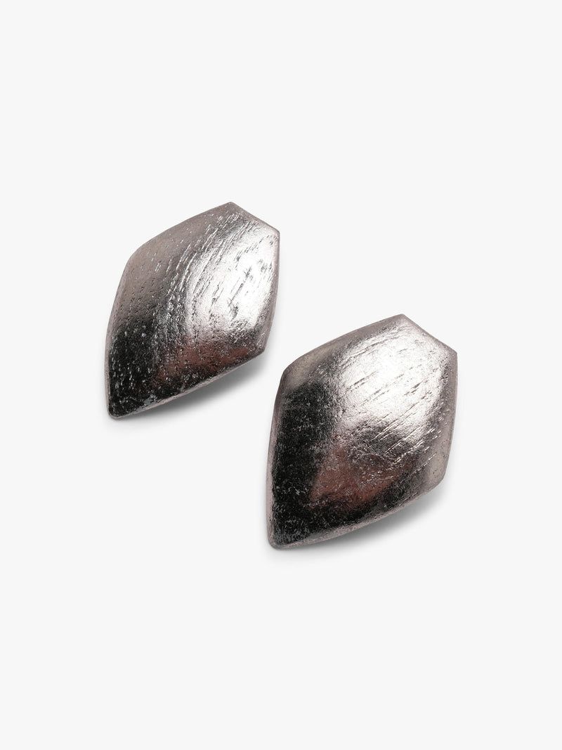 A pair of textured, metallic silver geometric stud earrings with a faceted, diamond-like shape, shown against a plain light gray background.