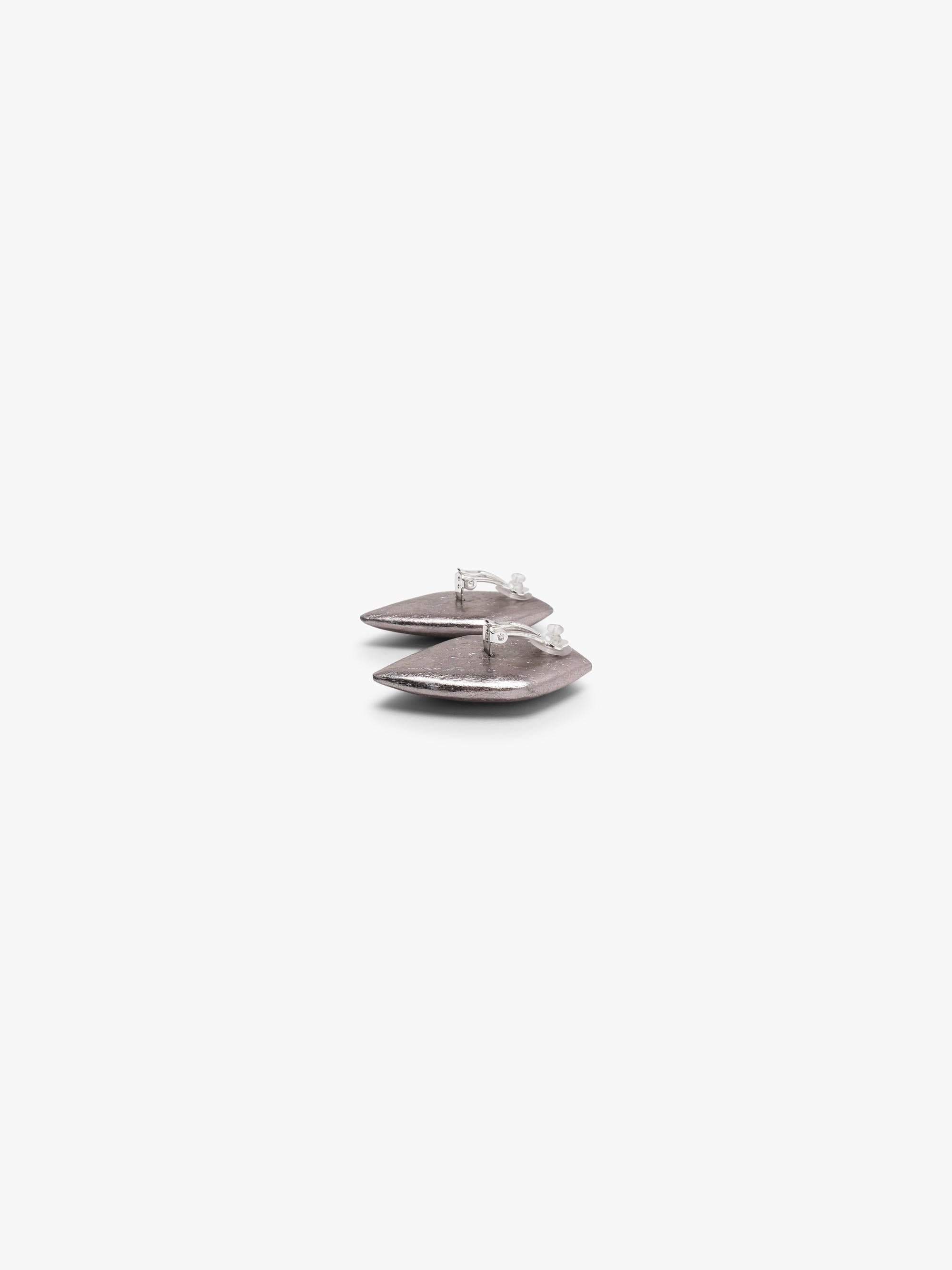 A pair of textured, metallic silver geometric stud earrings with a faceted, diamond-like shape, shown against a plain light gray background.