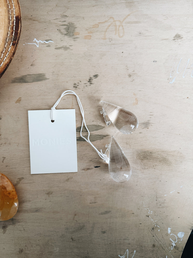 Clear acrylic nia earrings with a white tag on a wooden surface
