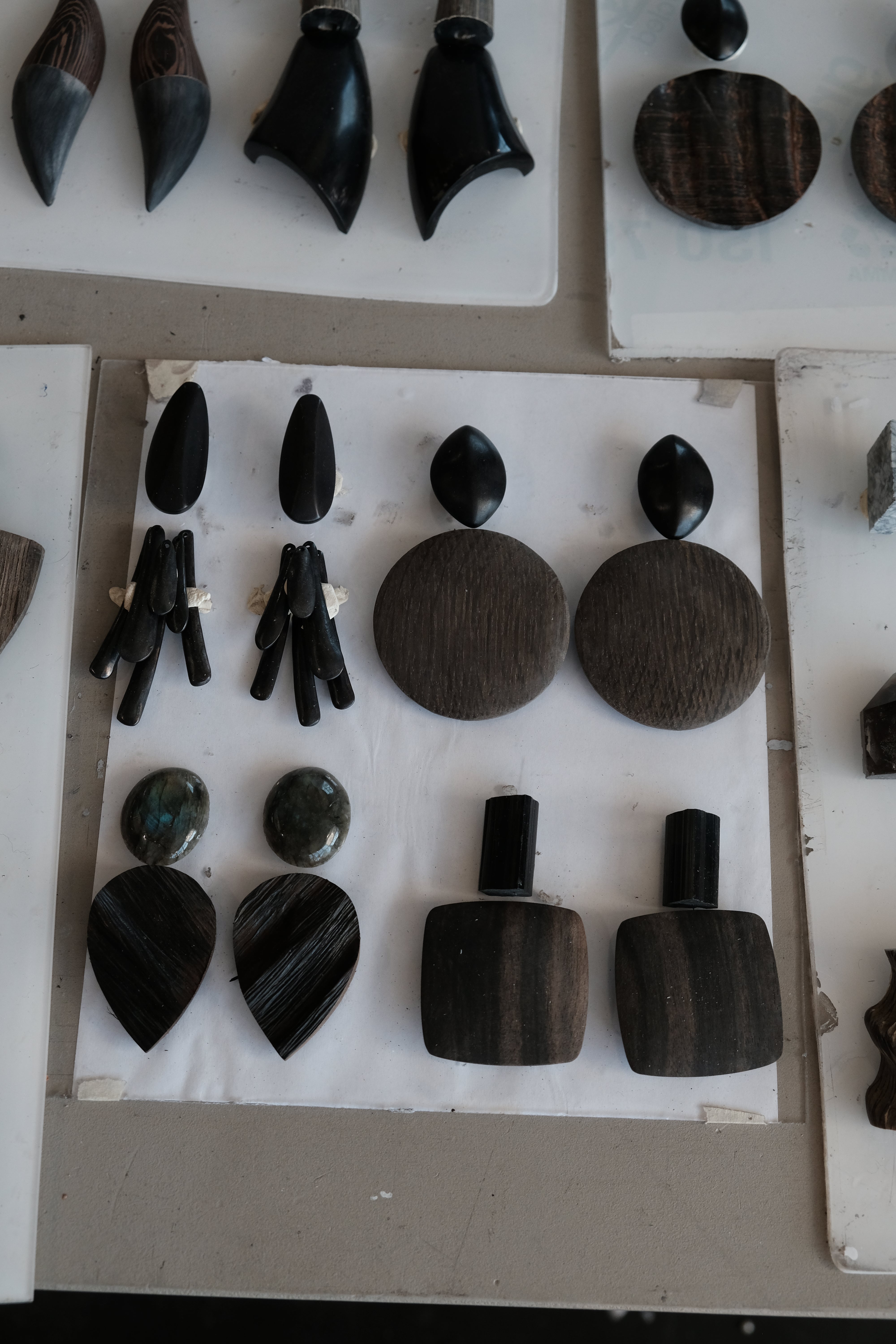 A display of handmade dark wood and stone jewelry, including wooden earrings, arranged on white backing boards.
