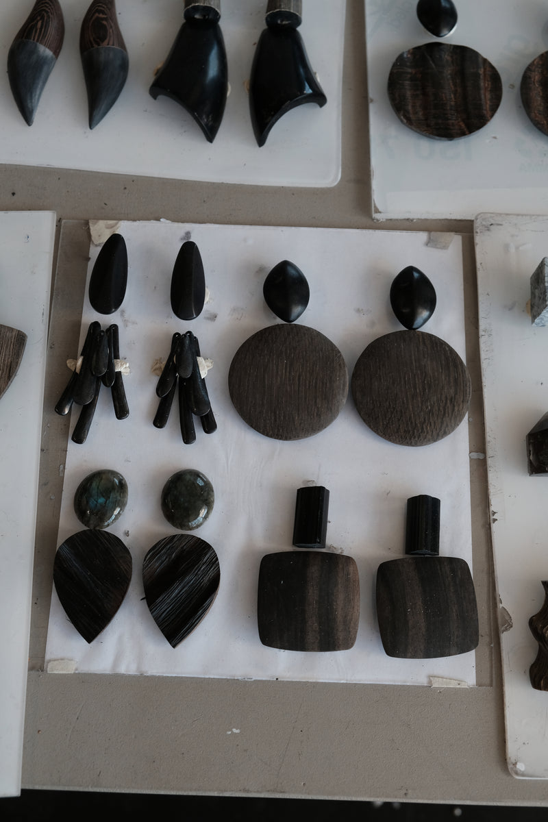 A display of handmade dark wood and stone jewelry, including wooden earrings, arranged on white backing boards.