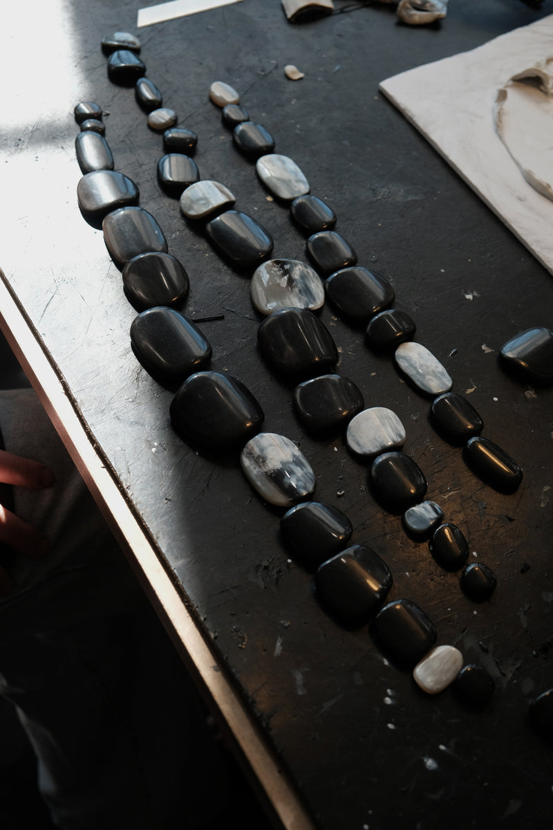 Several strands of polished black and white horn beads arranged on a dark workbench.