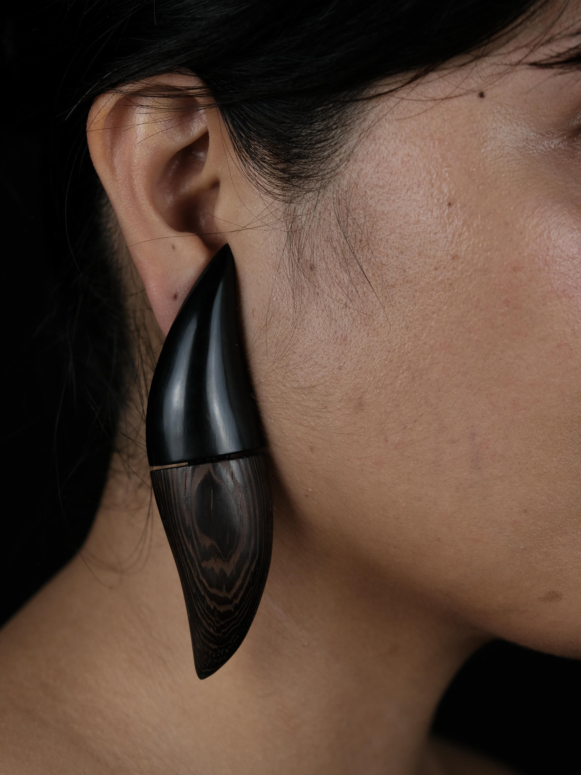 A close up of someones ear, wearing a black and brown curvy earring