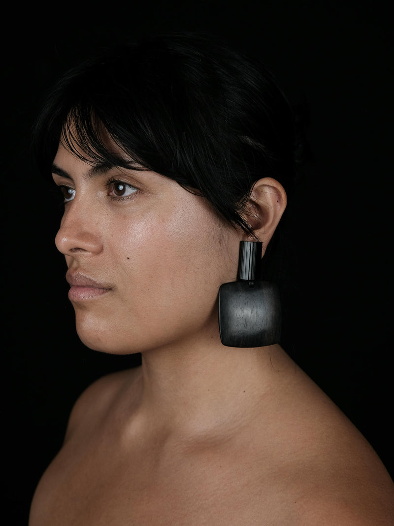 A sideprofile of a woman wearing a large, black  earring against a black background