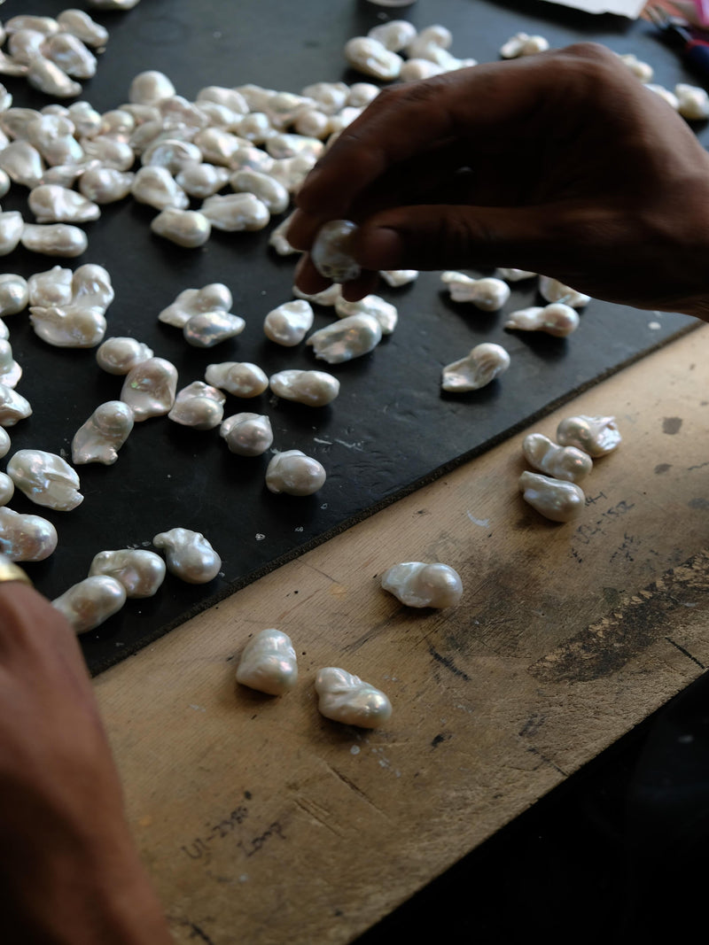 Close-up of hands working with baroque pearls on a dark surface.