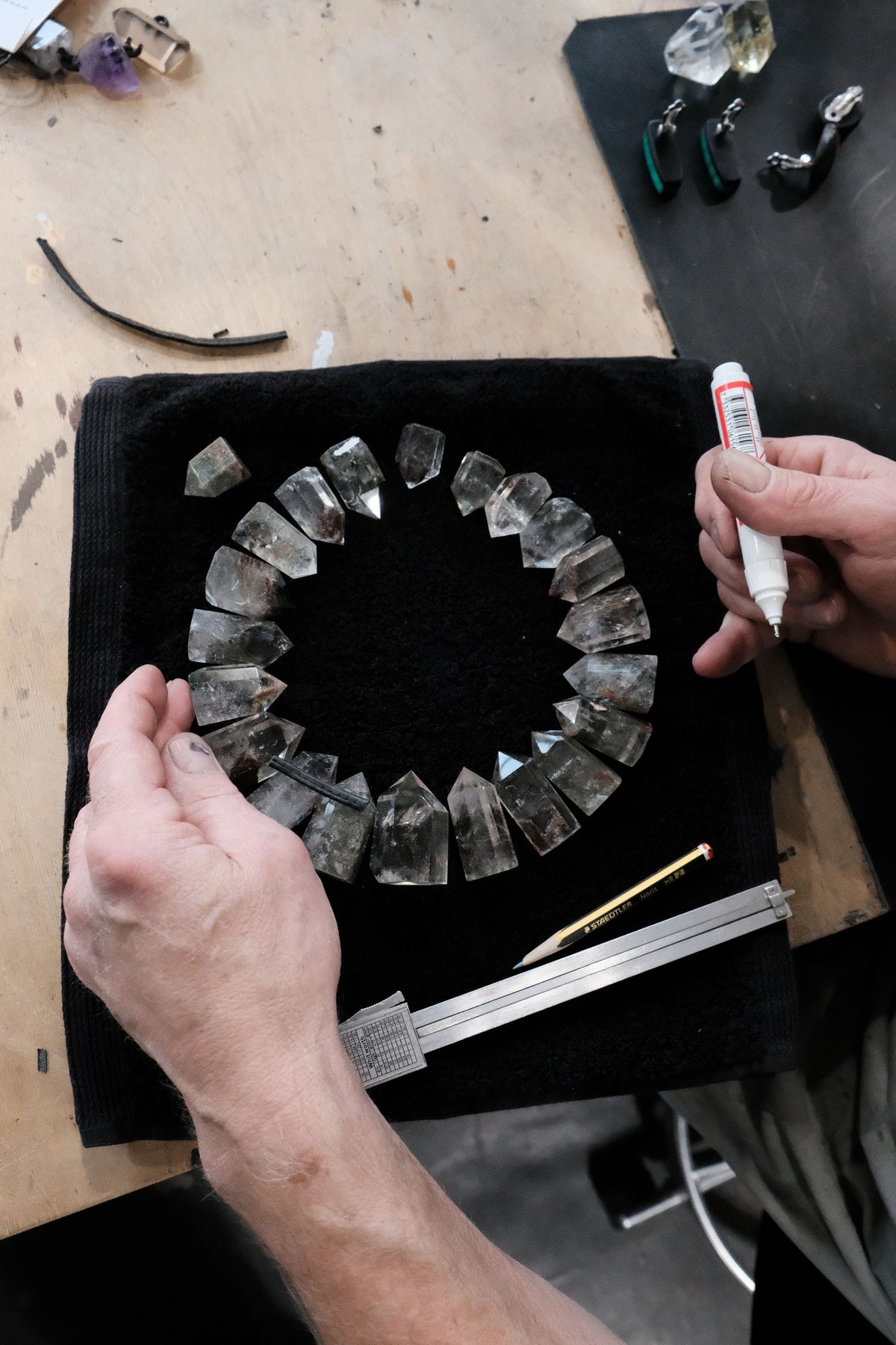 Person working on a crystal bracelet with tools on a wooden surface