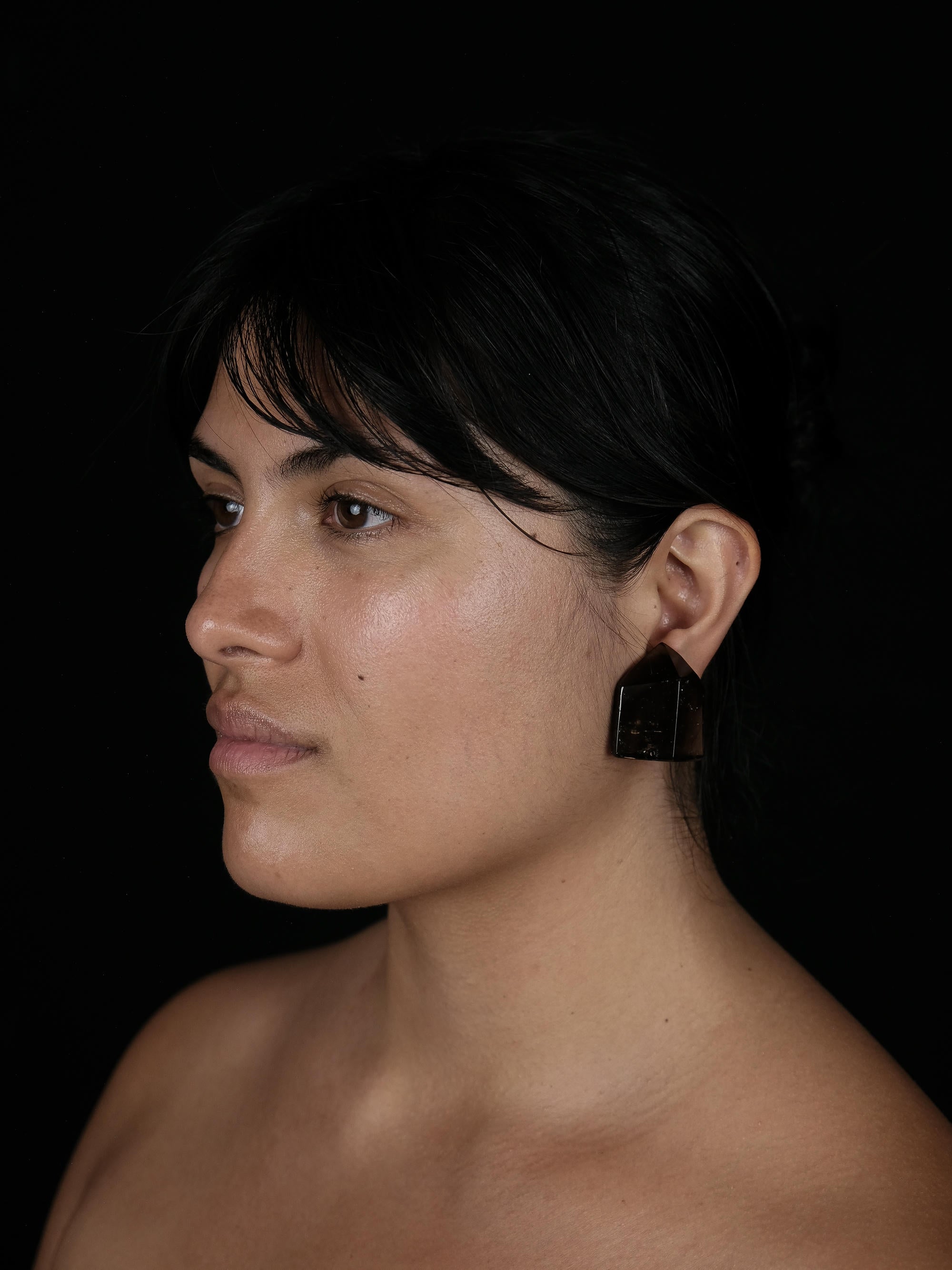 A side profile of a woman wearing faceted brown translucent earrings, against a black background