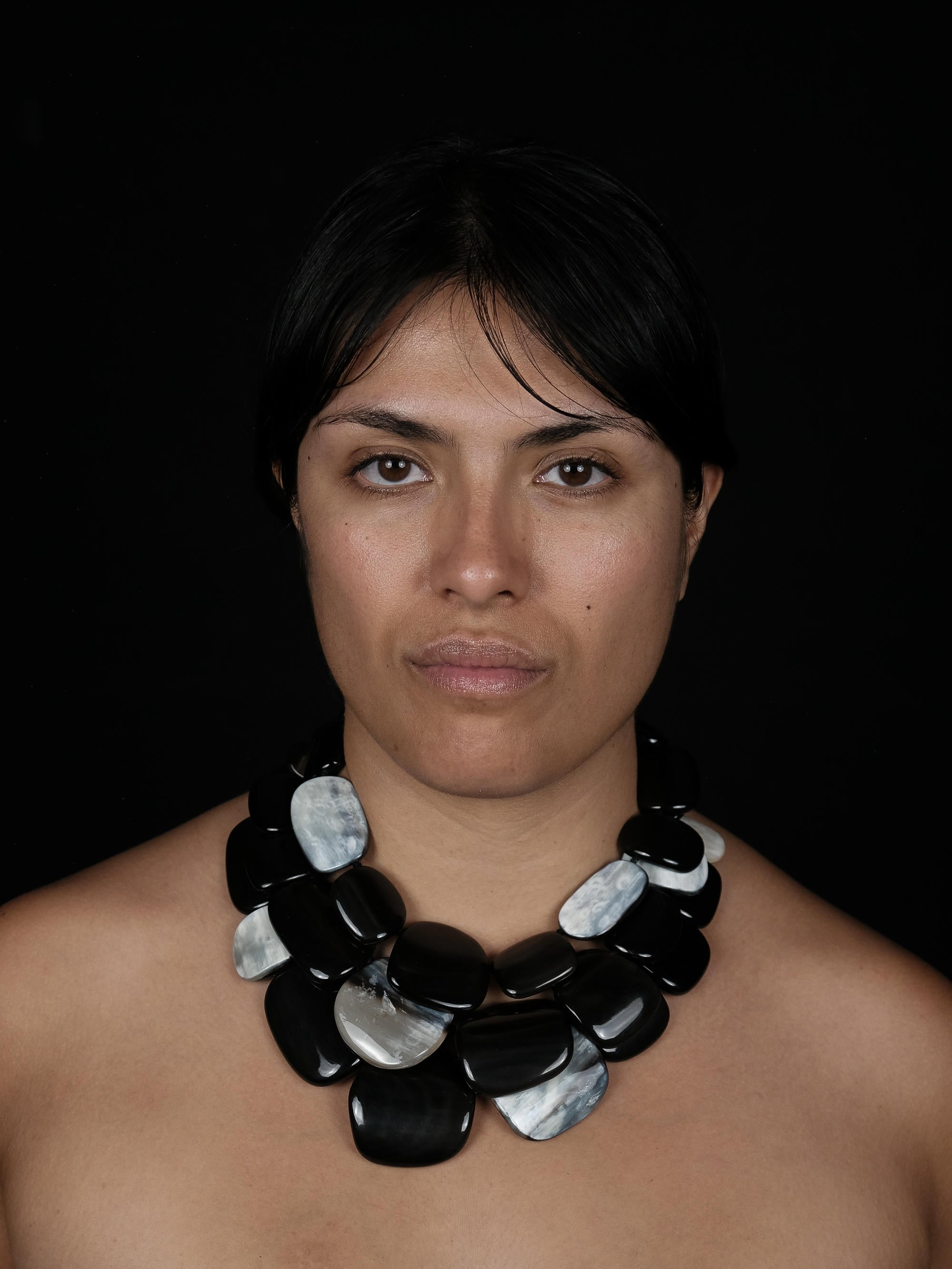 A woman wearing a multistrand necklace with black and greyish white pieces, against a black background