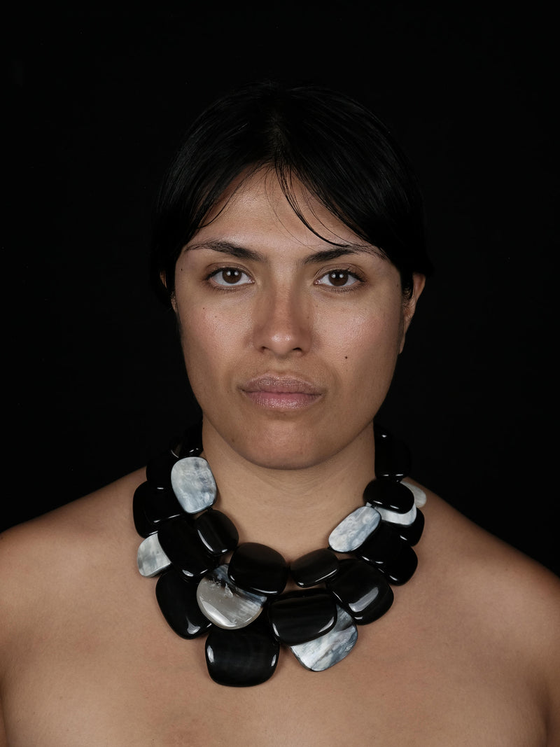 A woman wearing a multistrand necklace with black and greyish white pieces, against a black background