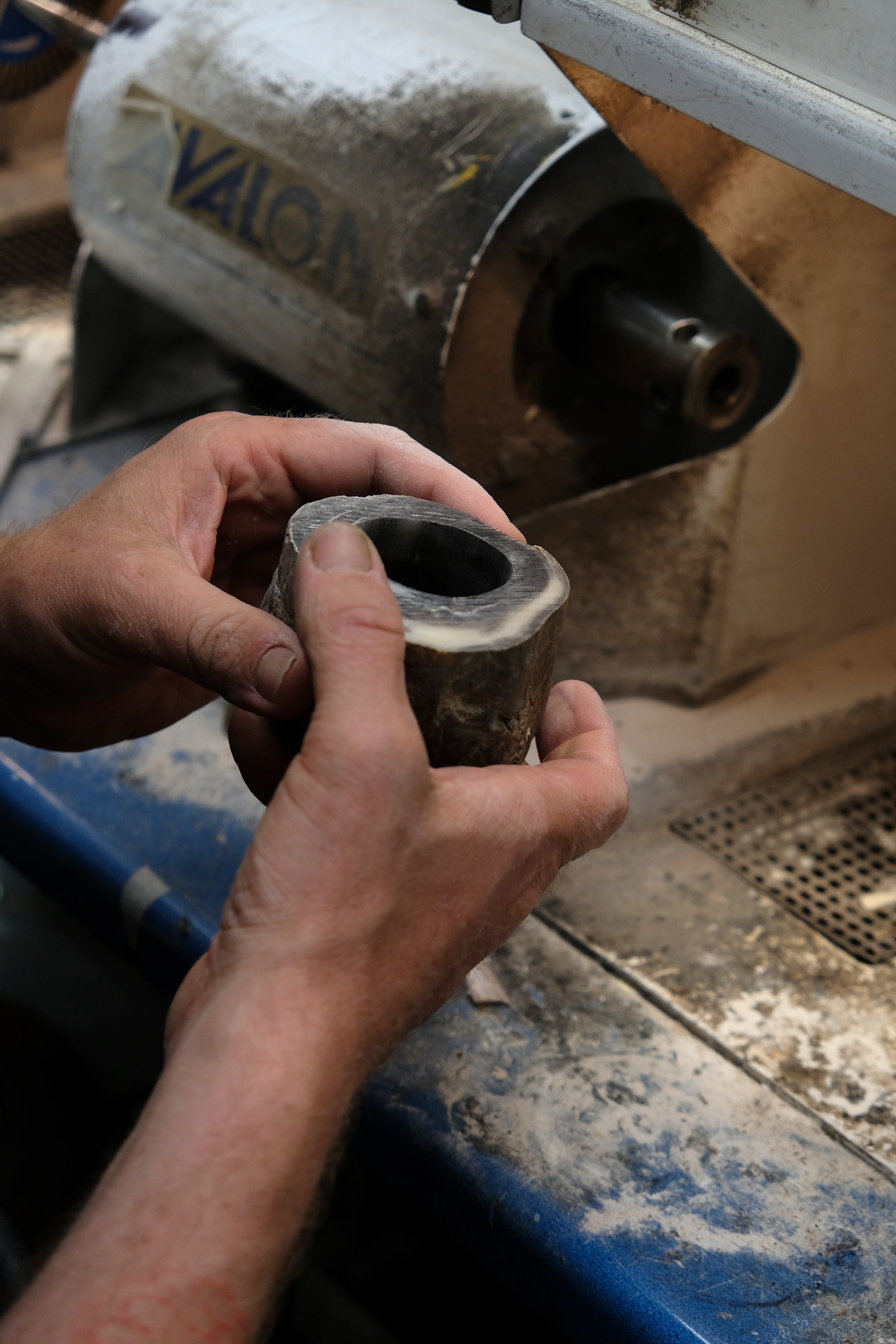 Person holding a cylindrical horn object with a machine in the background