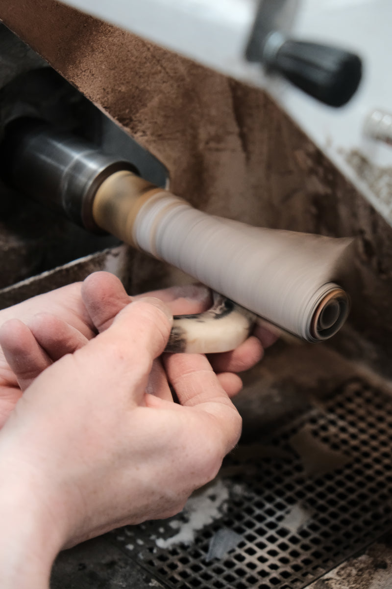 Person holding a cylindrical horn component near a machine with a brown towel underneath.