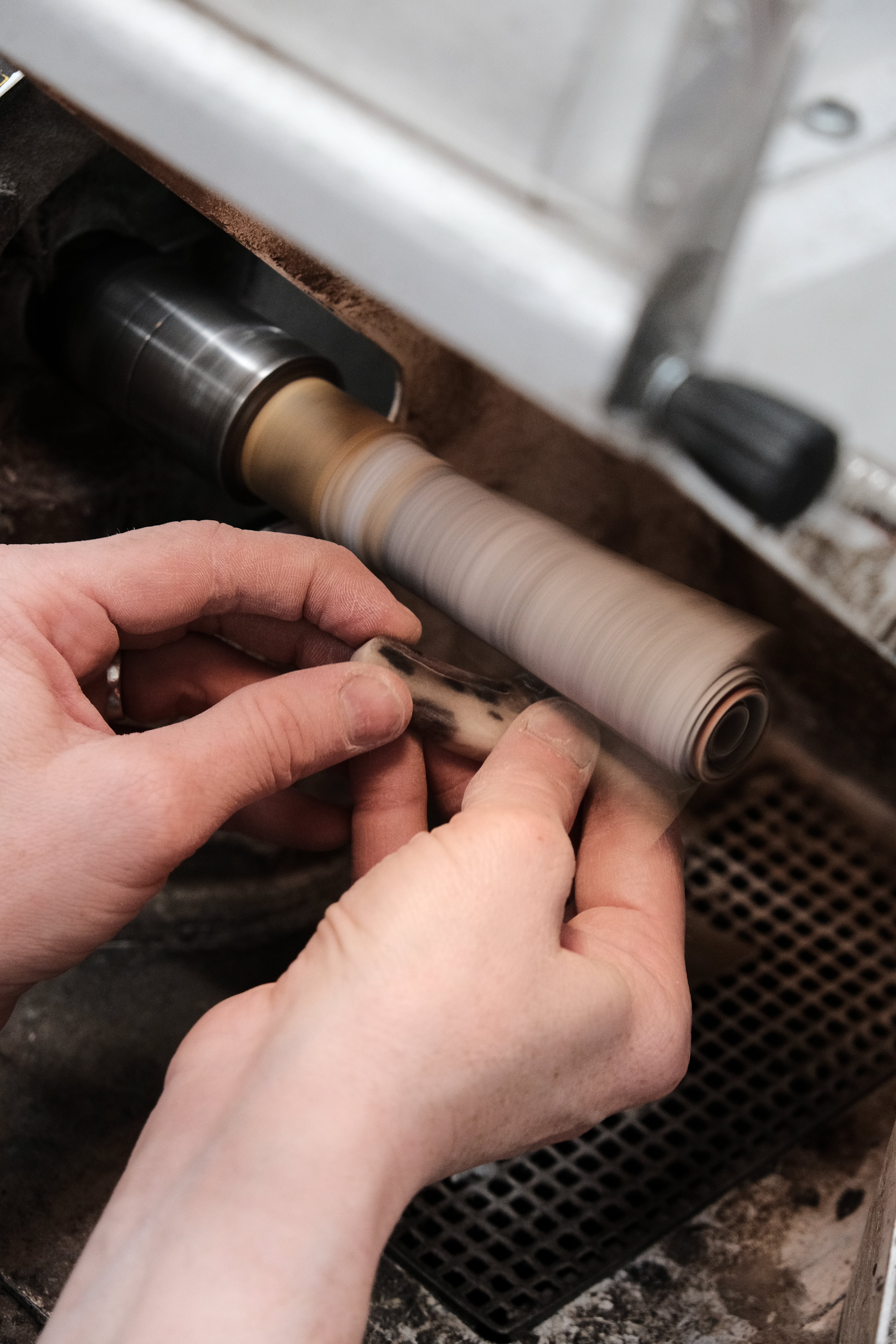 Person working on a mechanical component with a vehicle in the background