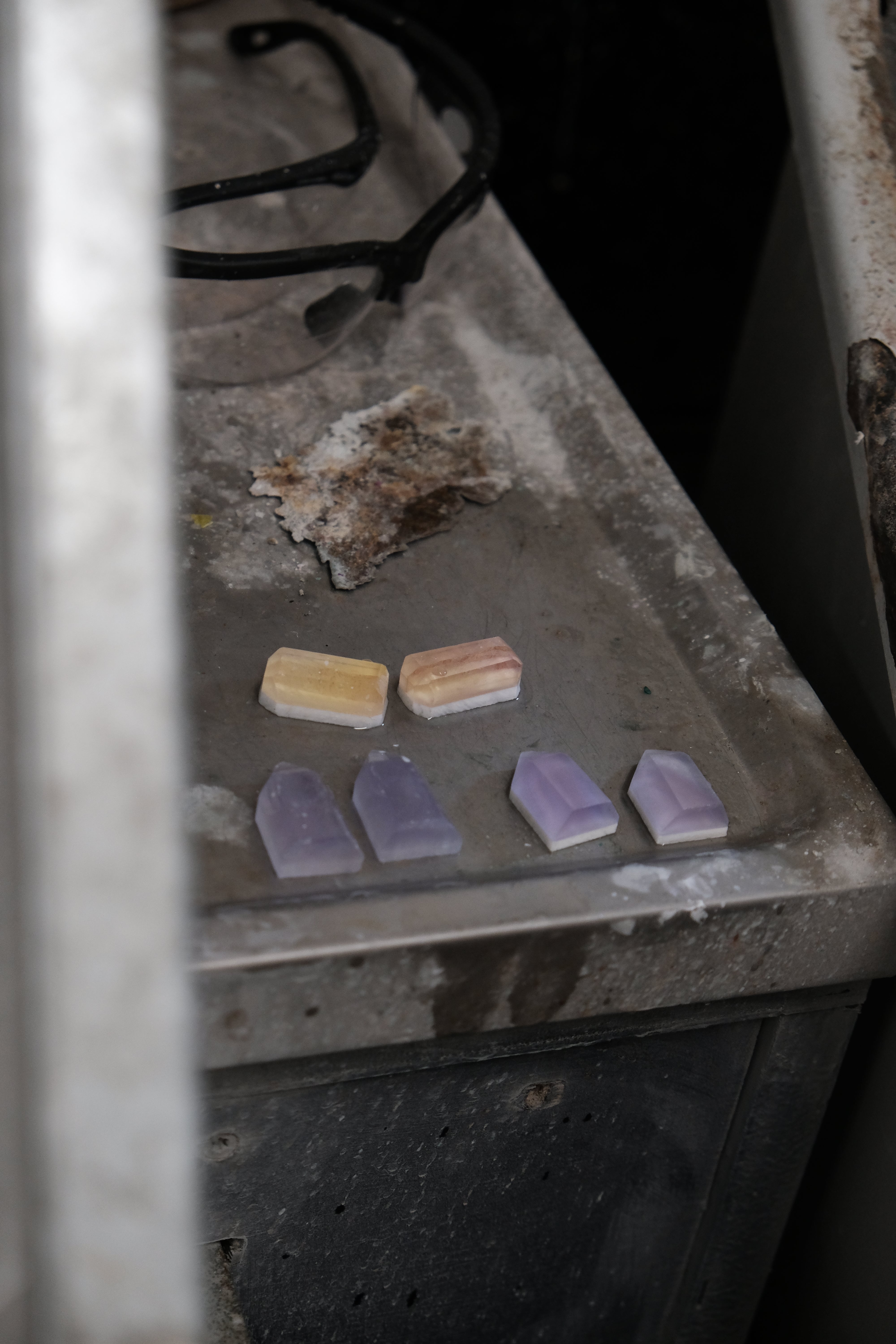 Five polished crystal or stone slices in pale lavender and cream tones arranged on a worn metal surface next to a dark stove area.