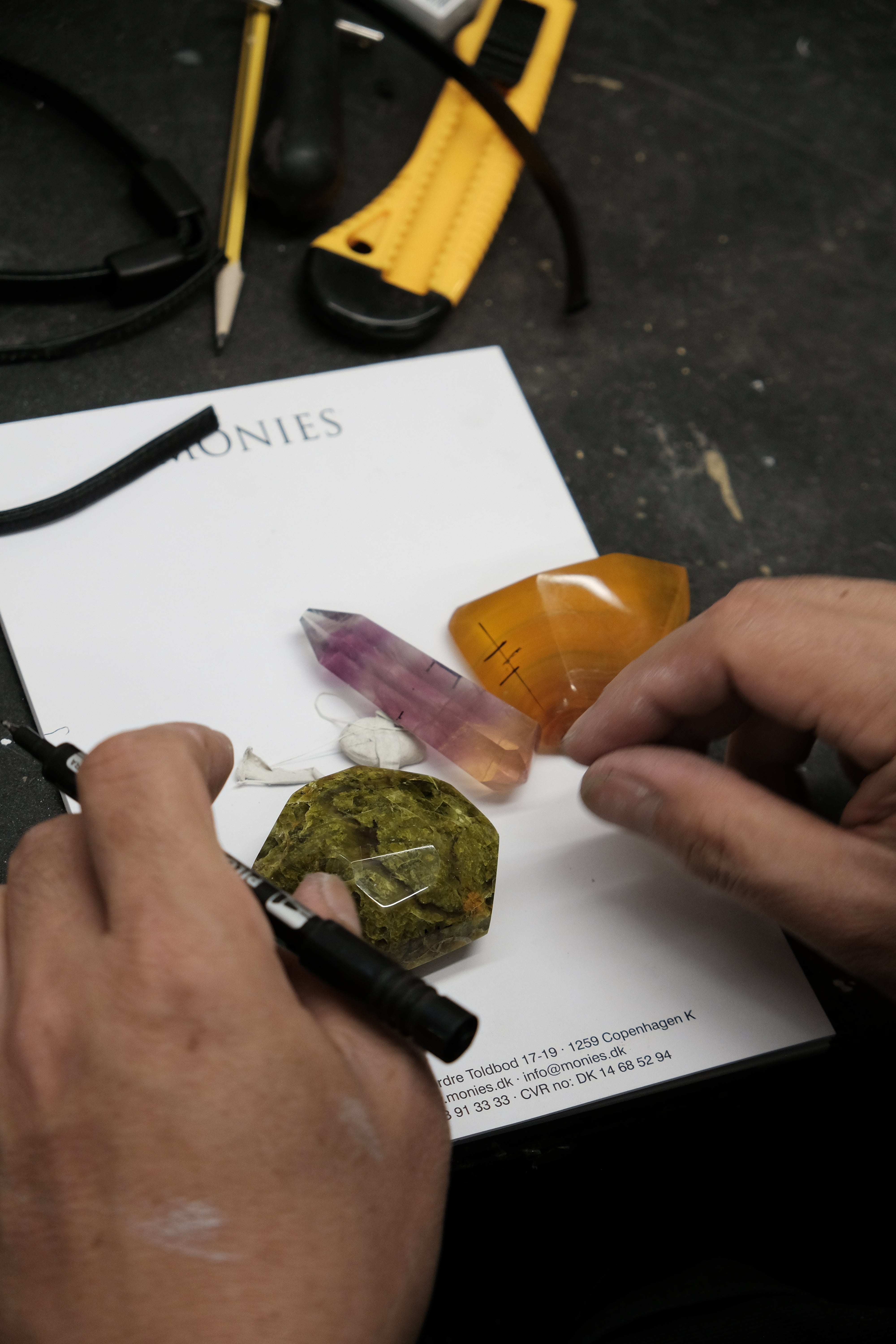Hands arranging natural stones in  green, purple and orange in a workshop environment. 