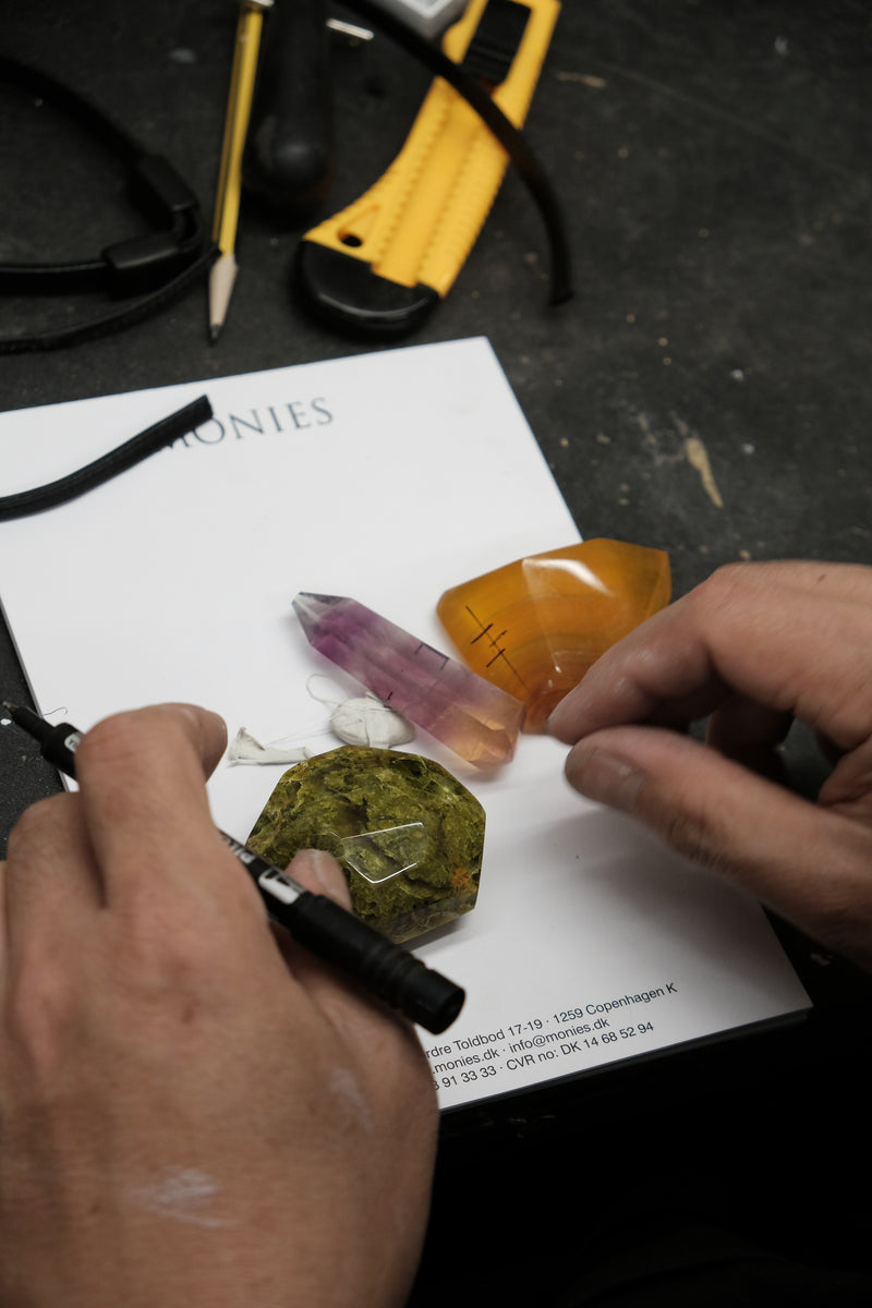 Hands arranging natural stones in  green, purple and orange in a workshop environment. 