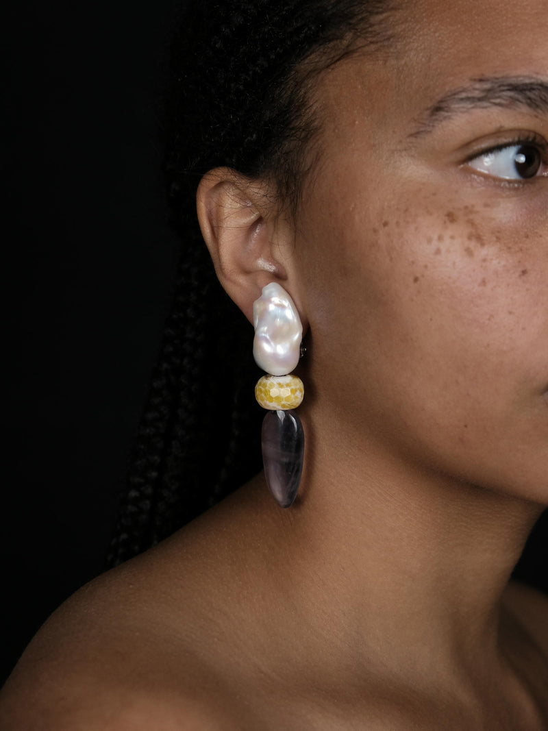 A woman wearing Baroque pearl earrings with rounded agate and ovalshaped flourite, displayed on a white background. 