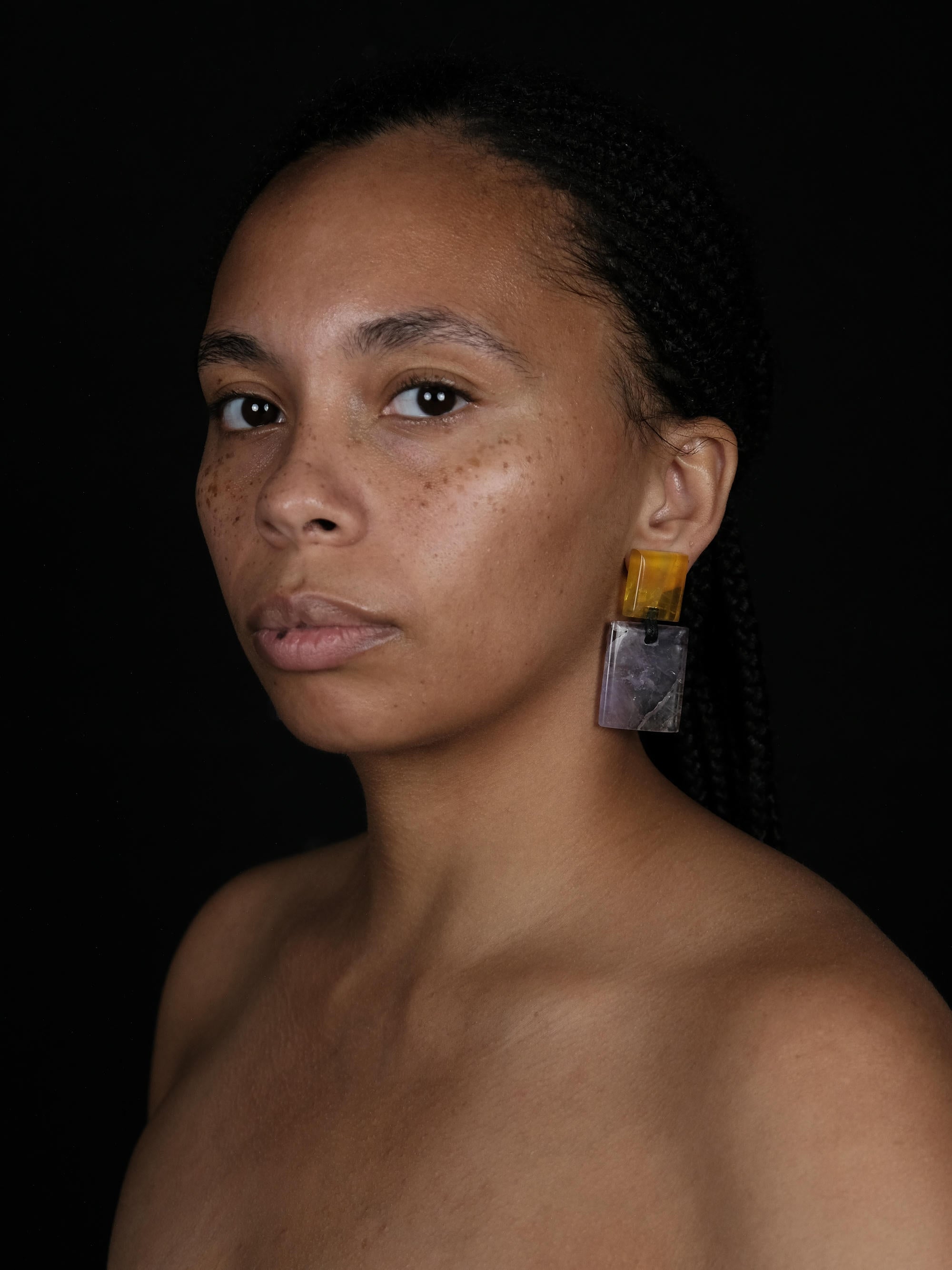 Model wearing earrings made of a small yellow square and a larger purple square underneath, displayed on a white background.