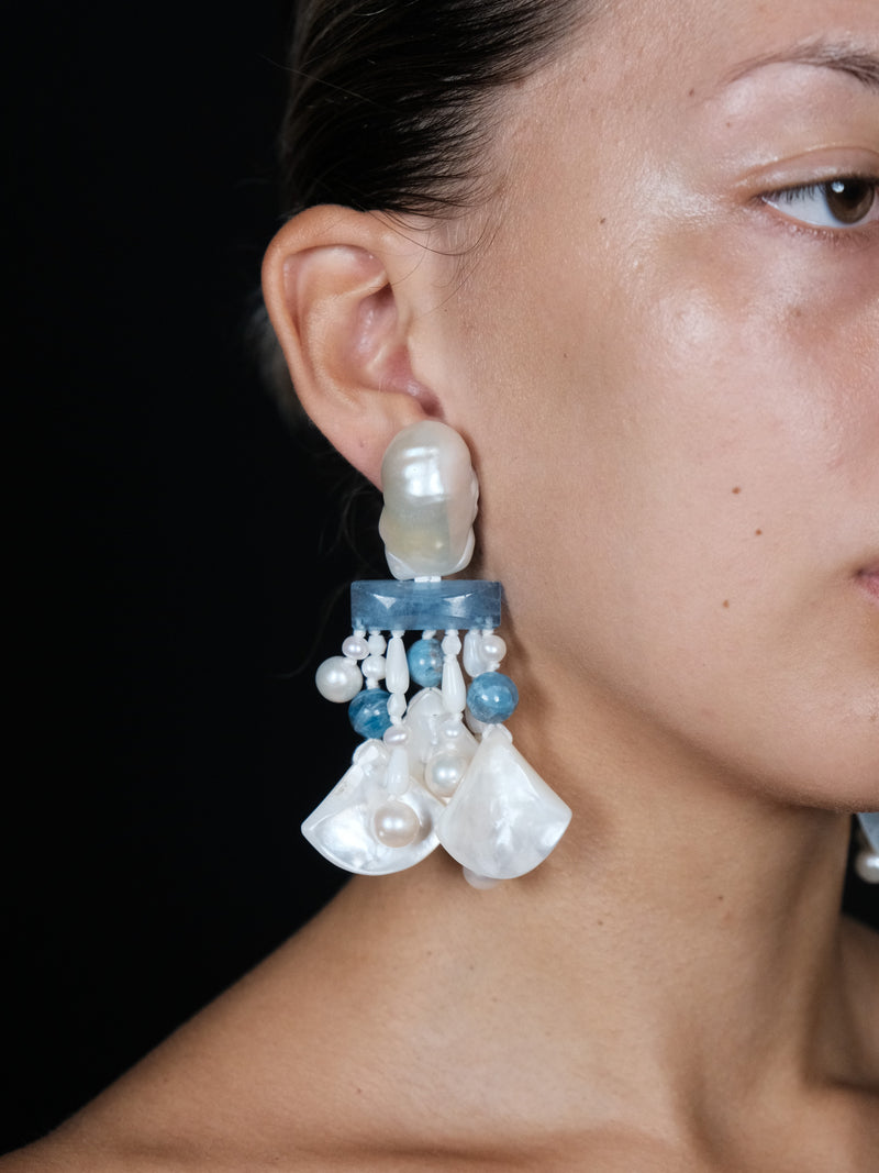 Close-up of a person wearing a detailed earring with pearls and blue accents.