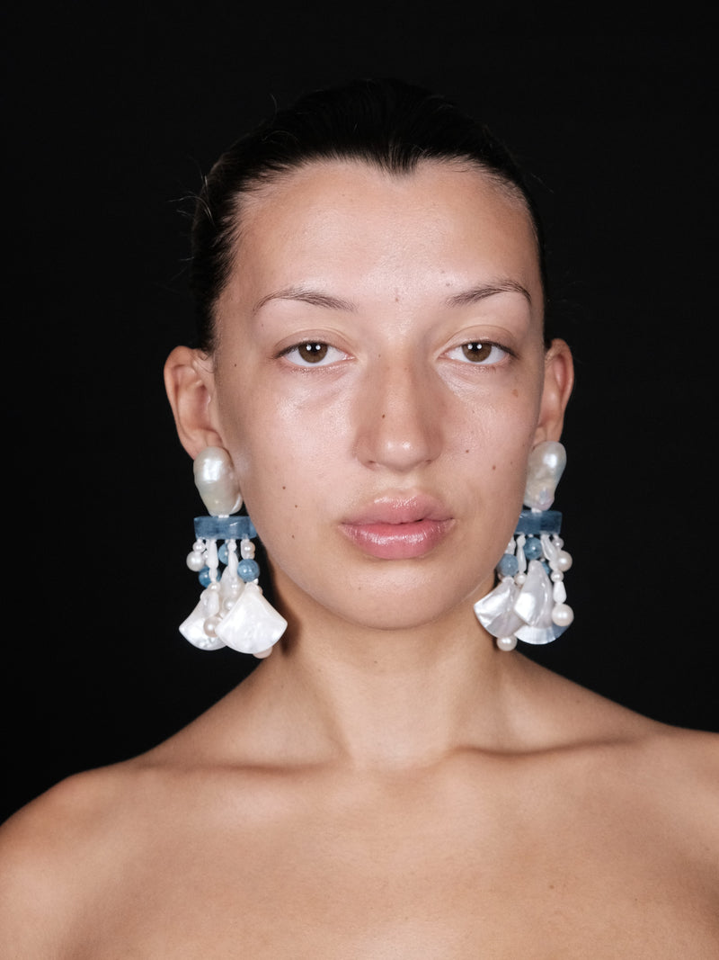 Woman wearing large, dangling earrings against a black background