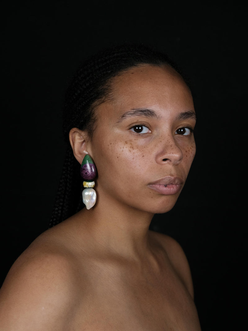 A close-up of a person's ear wearing a large, multi-colored statement earring made of polished green, purple, yellow, and white stones.