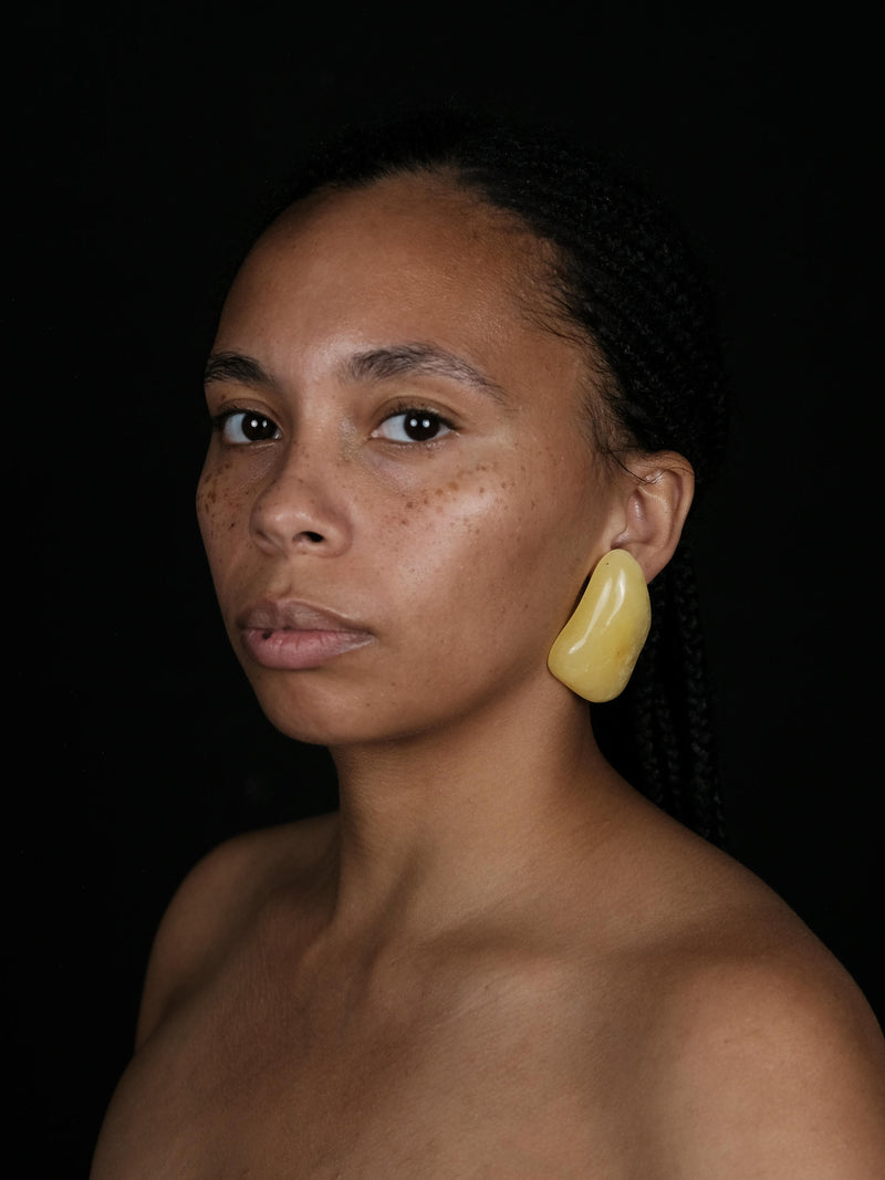 A woman wearing a  pair of irregular yellow amber earrings displayed on a white background