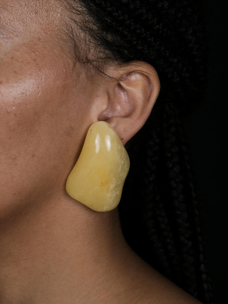 A close up of a woman wearing a  pair of irregular yellow amber earrings displayed on a white background
