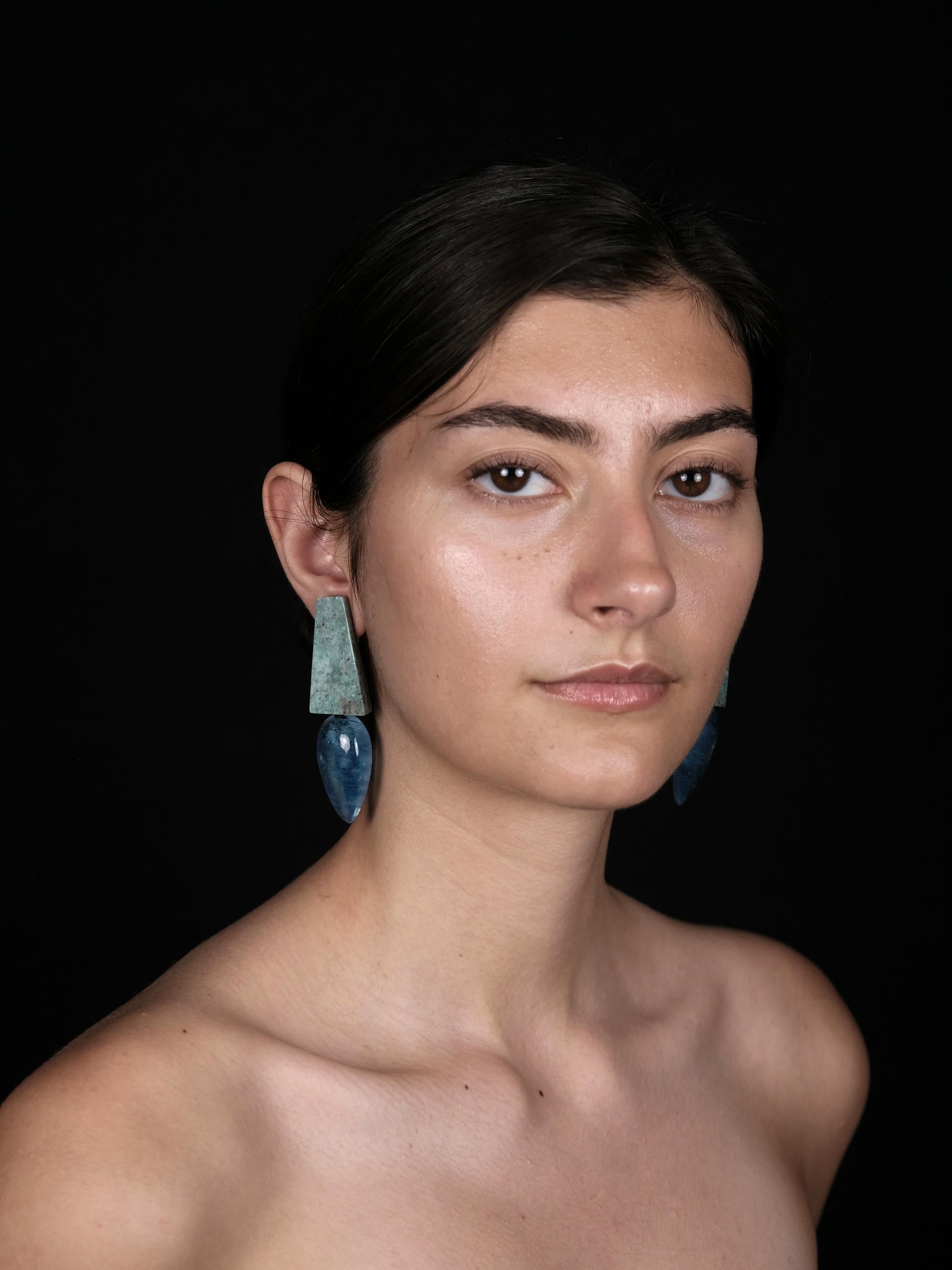 a person wearing long blue and green earrings against a black backgound