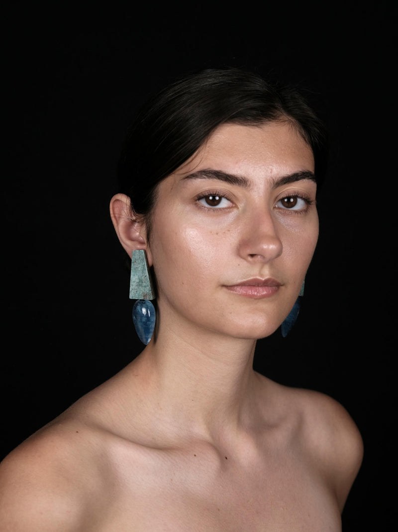 a person wearing long blue and green earrings against a black backgound