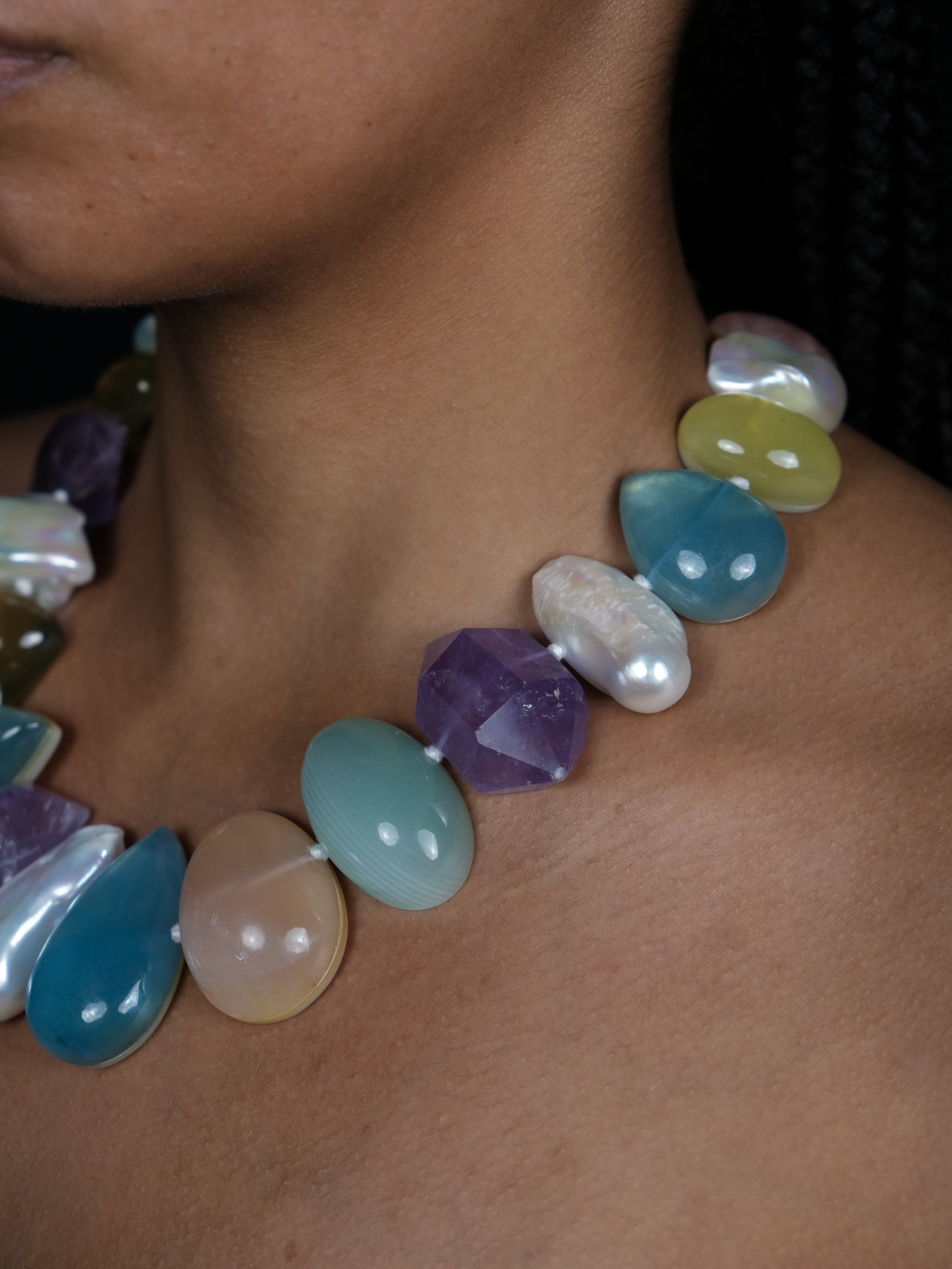 Close up of a woman wearing a single strand colorful necklace with green, blue, yellow beads and baroque pearls.