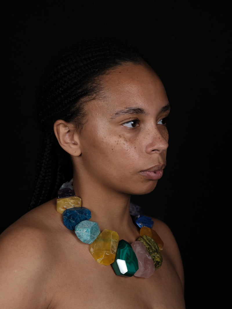 A woman wearing a colorful necklace, with Natural stones in blue, green, orange and pink. 